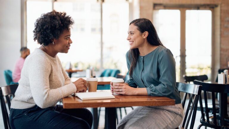A coach and client in a warm one-on-one conversation over coffee
